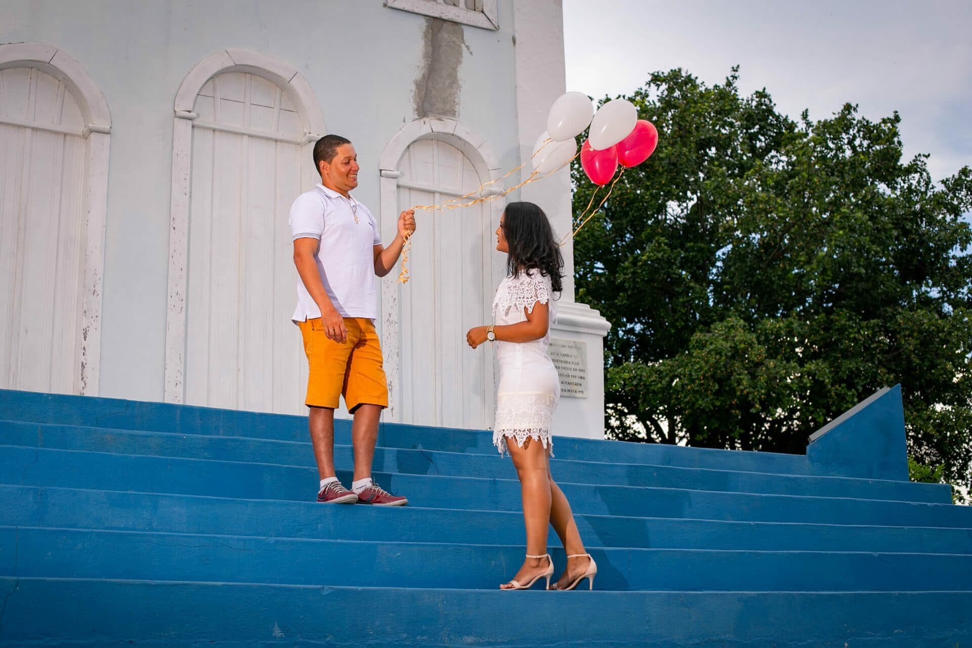 Casal com balões nos degraus azuis em frente à igreja.