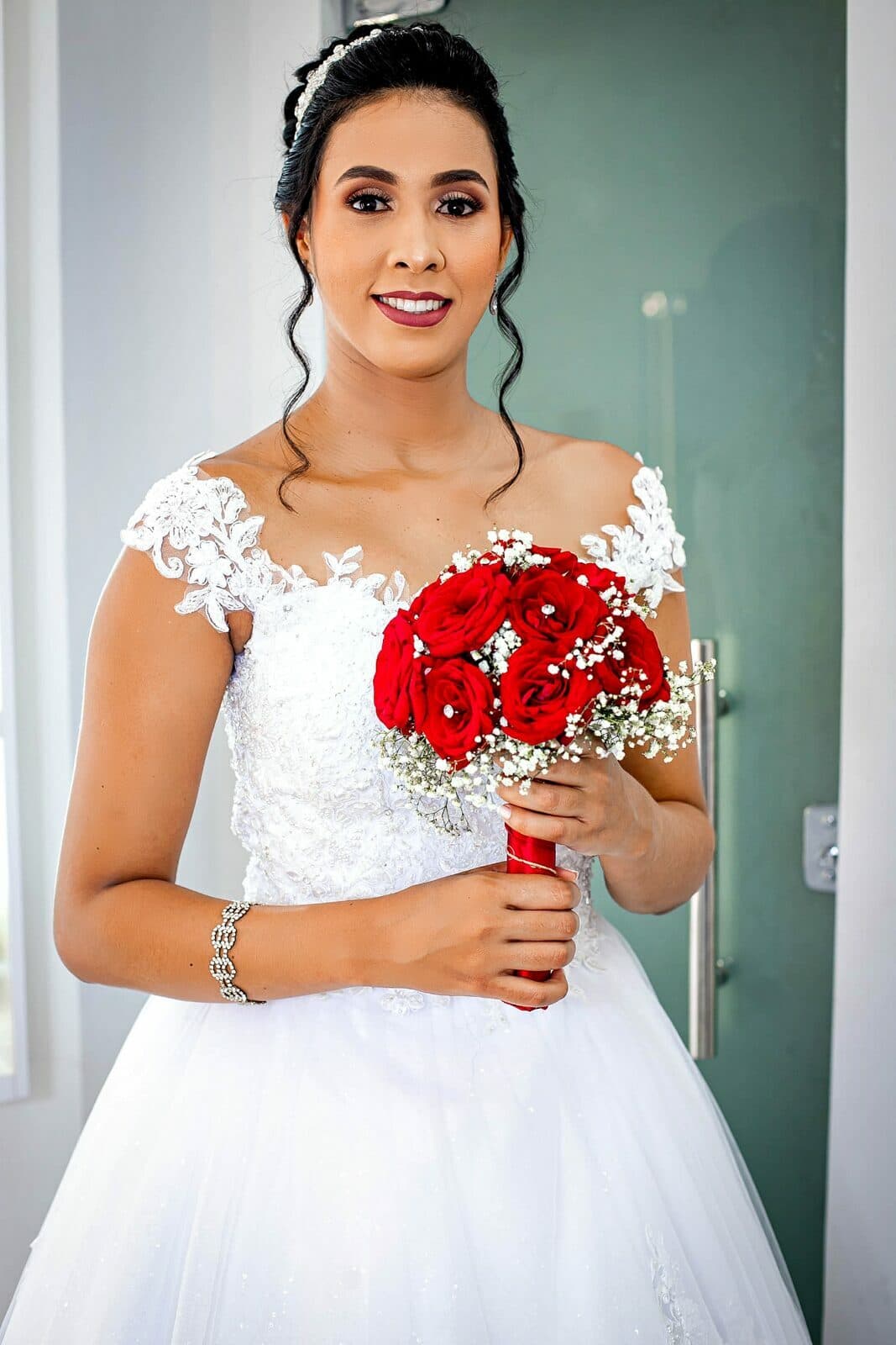 Noiva com buquê de rosas vermelhas em um retrato junto à porta.